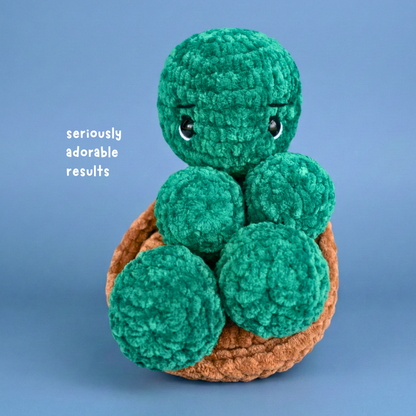 Handmade crocheted plush turtle with green textured body and brown shell on blue background