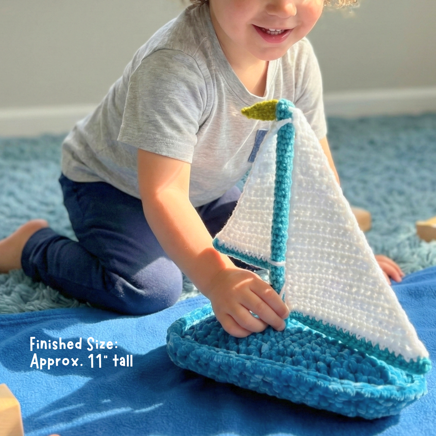 Child playing with a handmade crochet sailboat toy on a blue blanket indoors