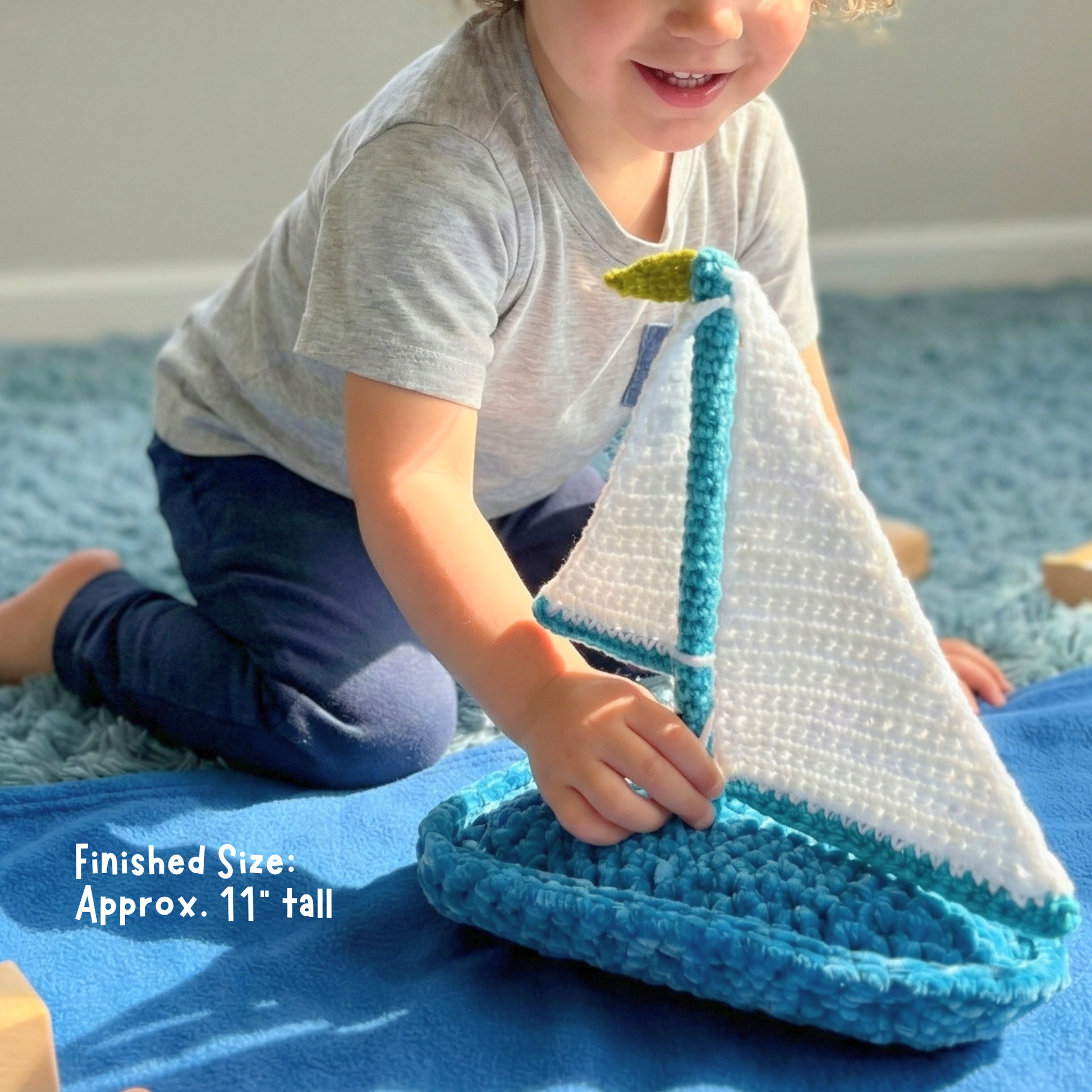 Child playing with a handmade crochet sailboat toy on a blue blanket indoors