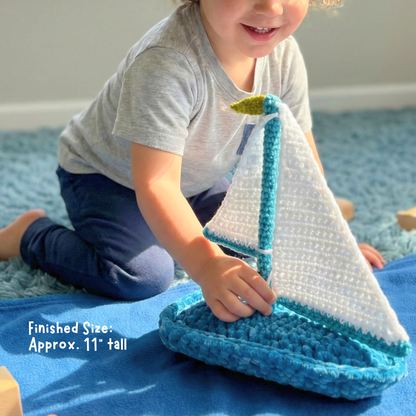 Child playing with a handmade crochet sailboat toy on a blue blanket indoors