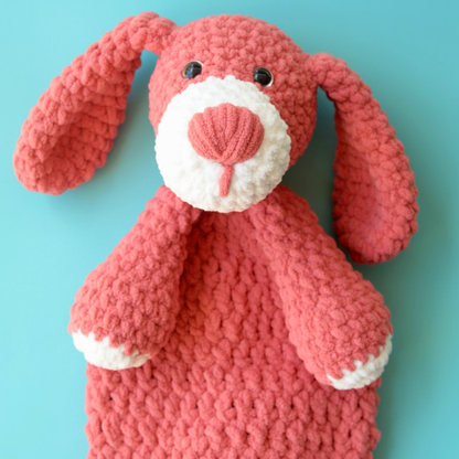 Handmade pink and white knitted dog plush toy with floppy ears on light blue background