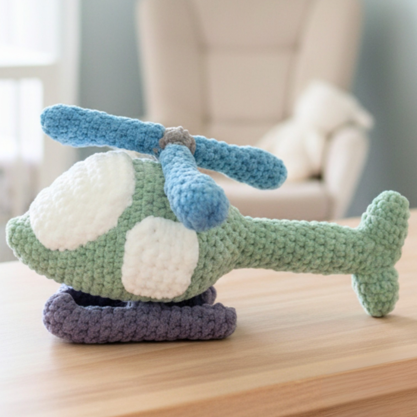 Handmade crocheted green toy helicopter with blue rotor blades on wooden table