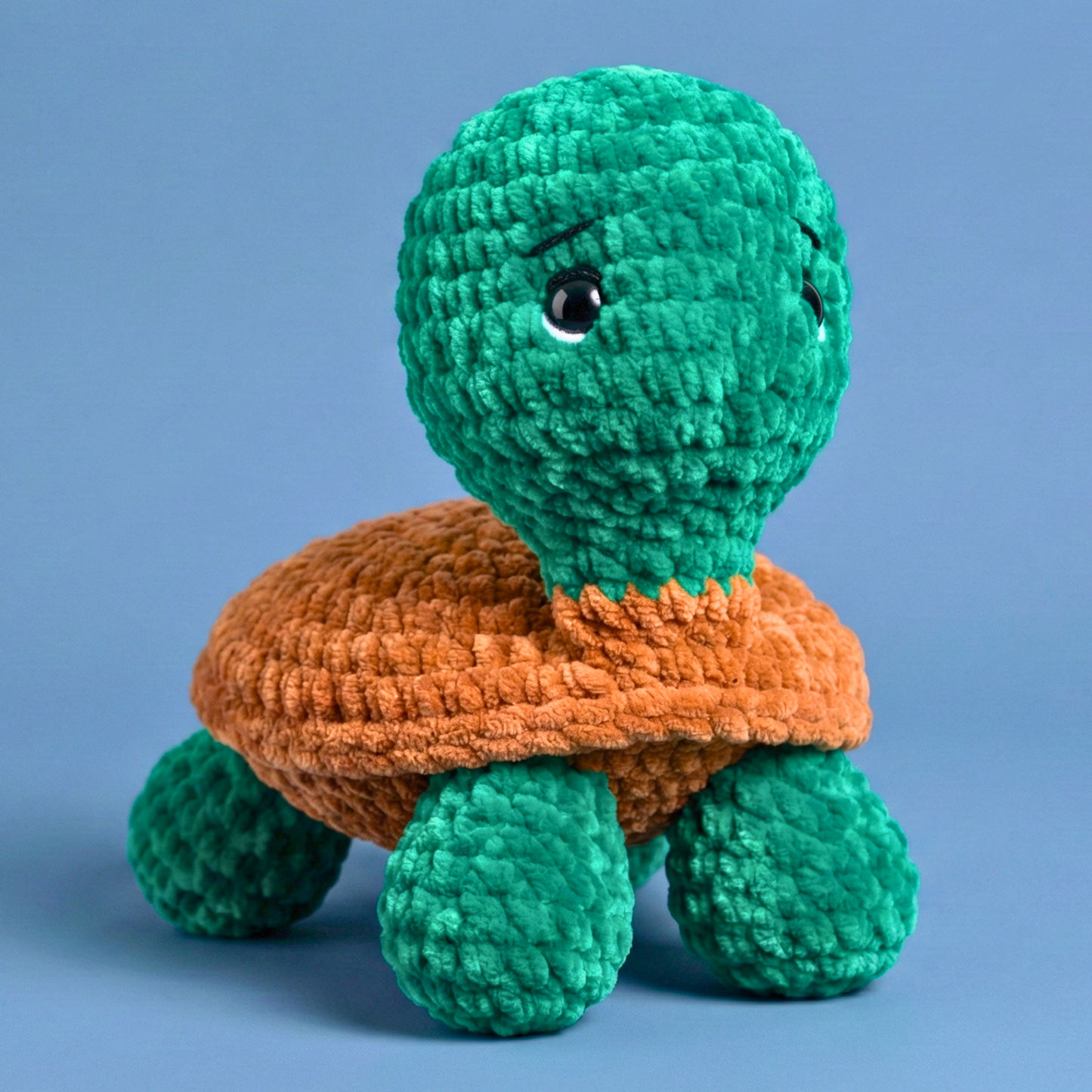 Handmade crochet plush turtle toy with green body and brown shell on blue background
