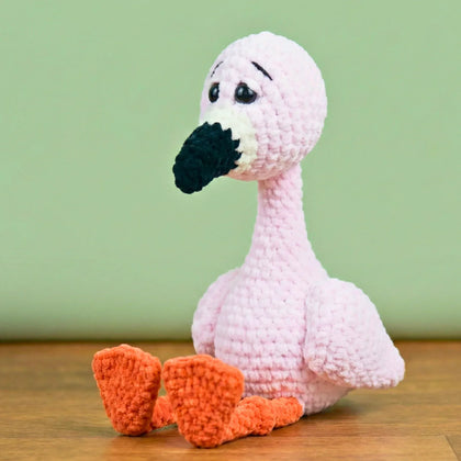 Pink crochet flamingo plushie with orange legs, amigurumi stuffed animal on wooden surface