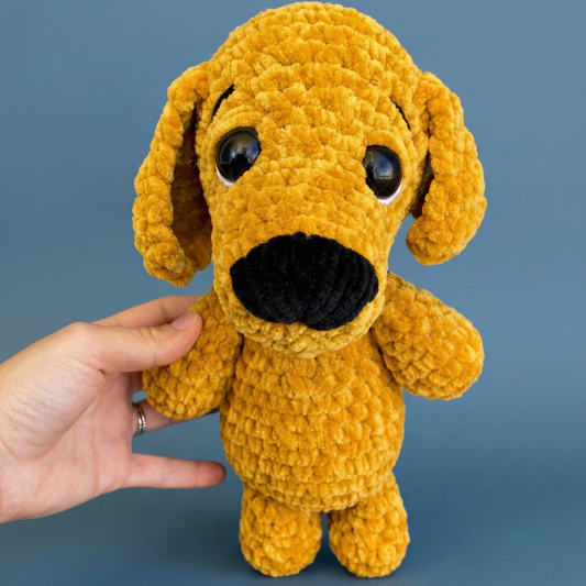 Hand holding a soft plush mustard yellow dog toy with big black eyes and a black nose against blue background