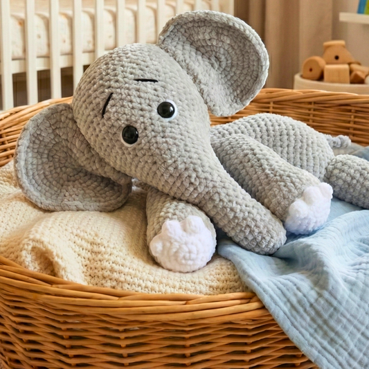 Handcrafted gray crocheted elephant plush toy resting in woven basket with knitted blankets