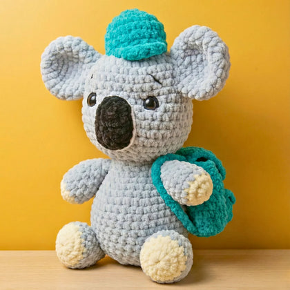 Crochet koala stuffed animal with teal hat and backpack, amigurumi plushie on yellow background
