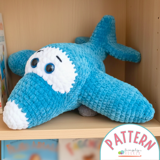 Blue plush airplane toy on a shelf with 'Simply Hooked' pattern label.