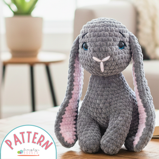 Gray crochet bunny toy with long ears on a wooden surface, with 'Pattern' logo in the corner.