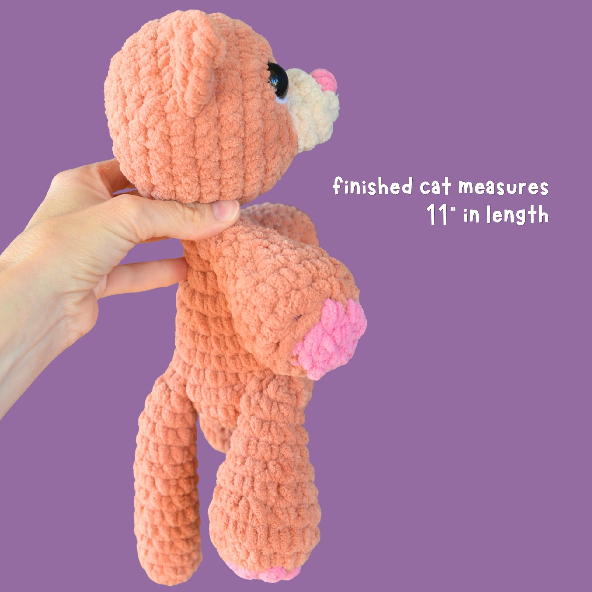 Hand holding a pink crochet cat toy against a purple background with text indicating size.