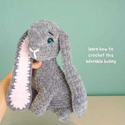 Hand holding gray chunky yarn crochet bunny with long ears and soft pink inner ear.