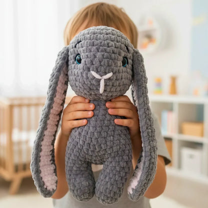 Child holding a chunky yarn crochet bunny plushie with long floppy ears in a cozy room
