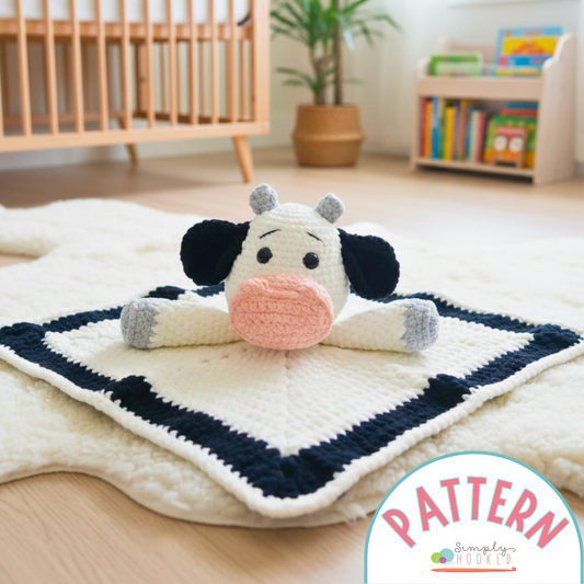 Crocheted cow toy on a blanket in a room with a crib and books.