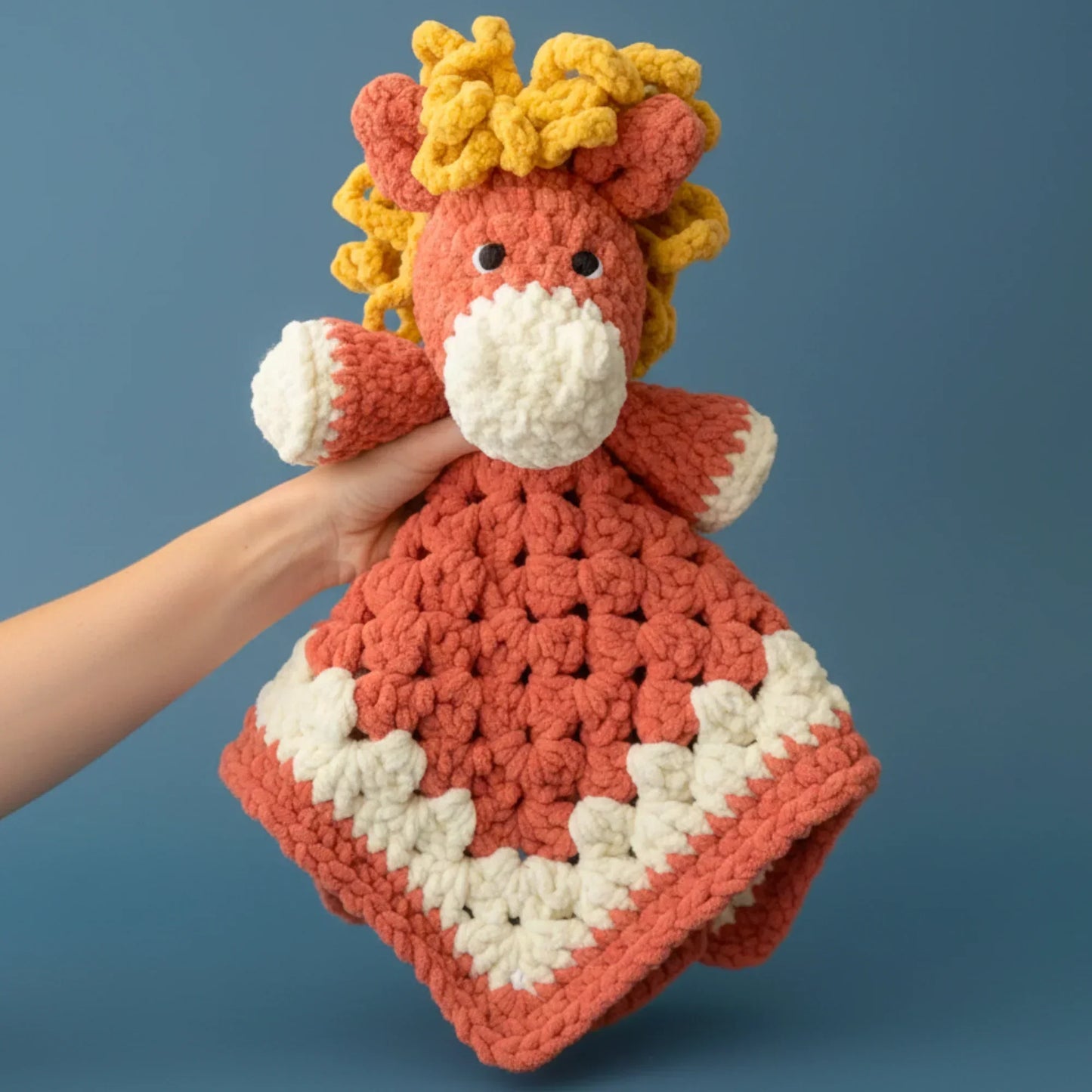 Hand holding a red and cream crochet horse blanket plushie with a yellow mane