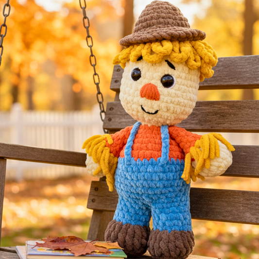 crochet scarecrow plushie with yellow yarn hair, blue overalls and brown hat on bench outdoors