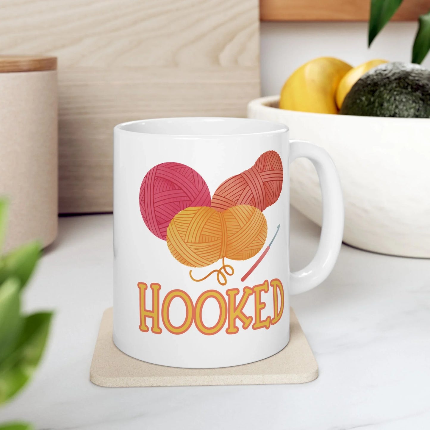 White mug with yarn ball design and 'HOOKED' text on a white surface.