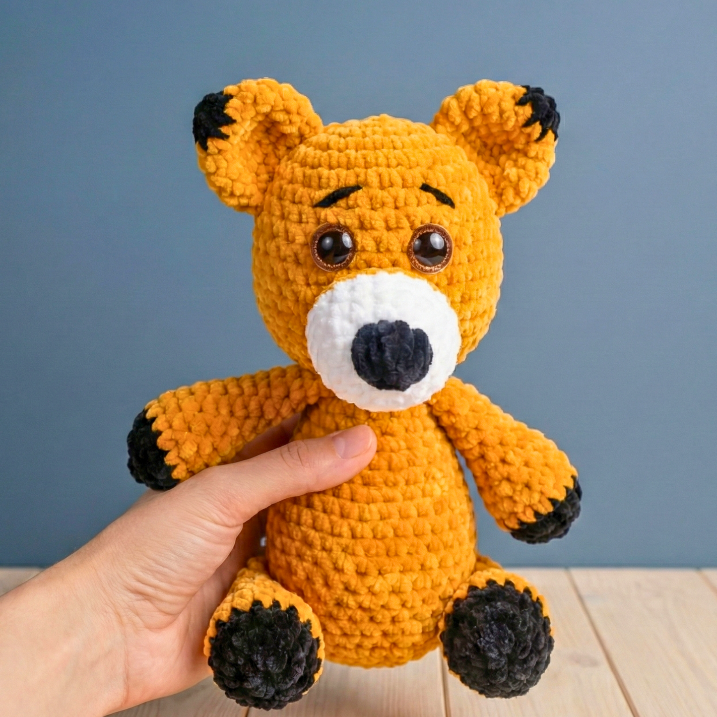 Hand holding a small orange fox toy against a blue background