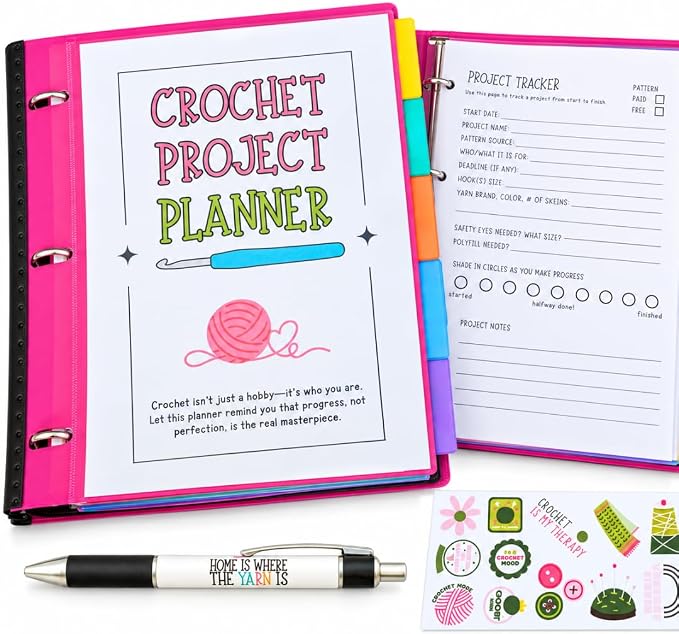 A crochet project planner set shown open in a bright pink binder, with a printed cover page reading 'Crochet Project Planner,' an interior project tracker sheet, a black-and-white pen printed with 'Home is where the craft is,' and several small decorative sticker sheets on a white background.