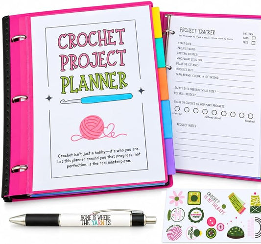 A crochet project planner set shown open in a bright pink binder, with a printed cover page reading 'Crochet Project Planner,' an interior project tracker sheet, a black-and-white pen printed with 'Home is where the craft is,' and several small decorative sticker sheets on a white background.