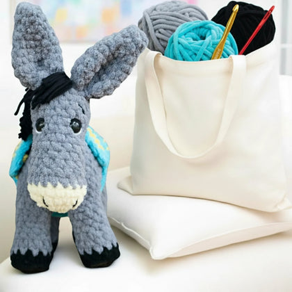 Crochet donkey plushie with blue yarn bag and crochet hooks, amigurumi pattern scene