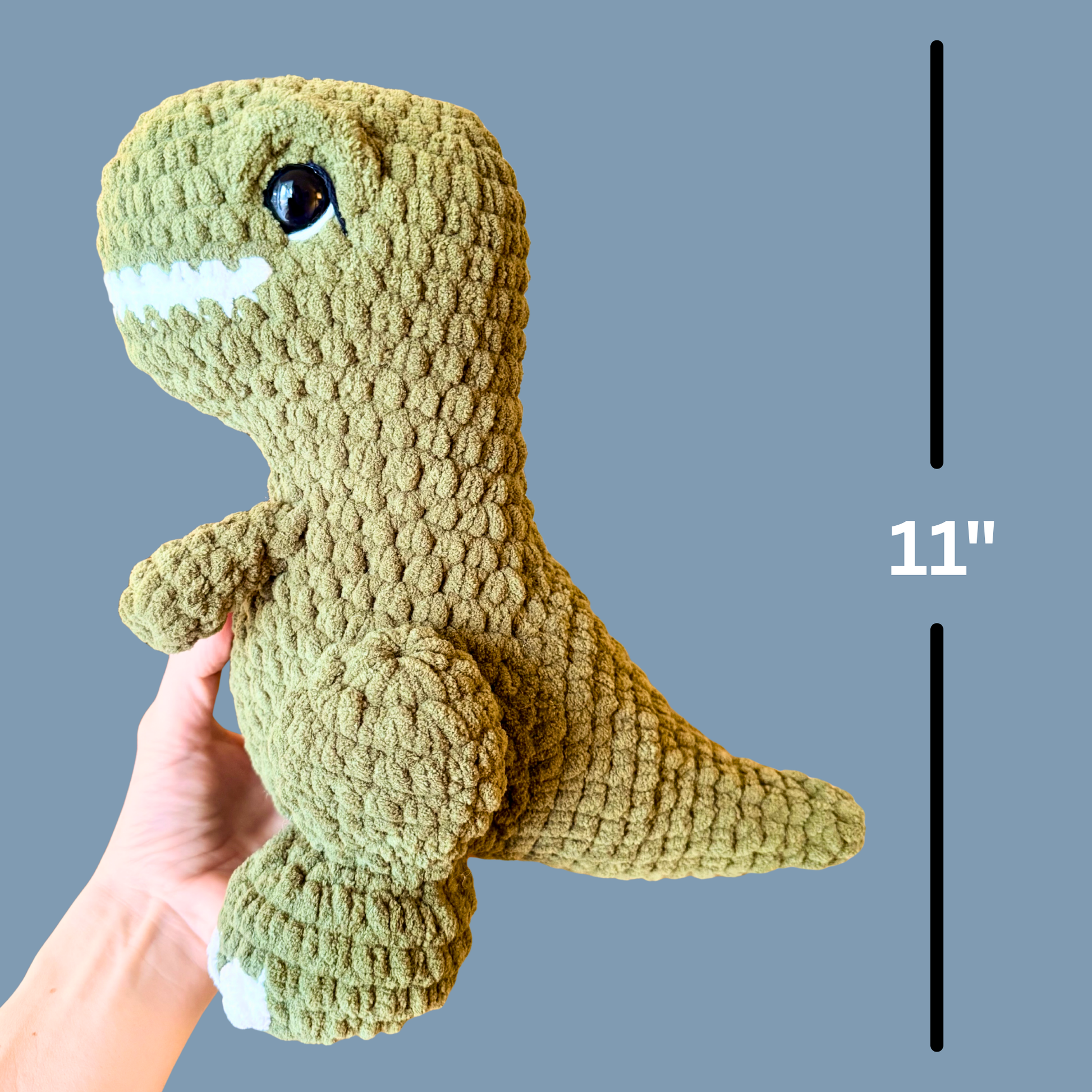 Crocheted dinosaur toy held by a hand with a measurement label on a gray background