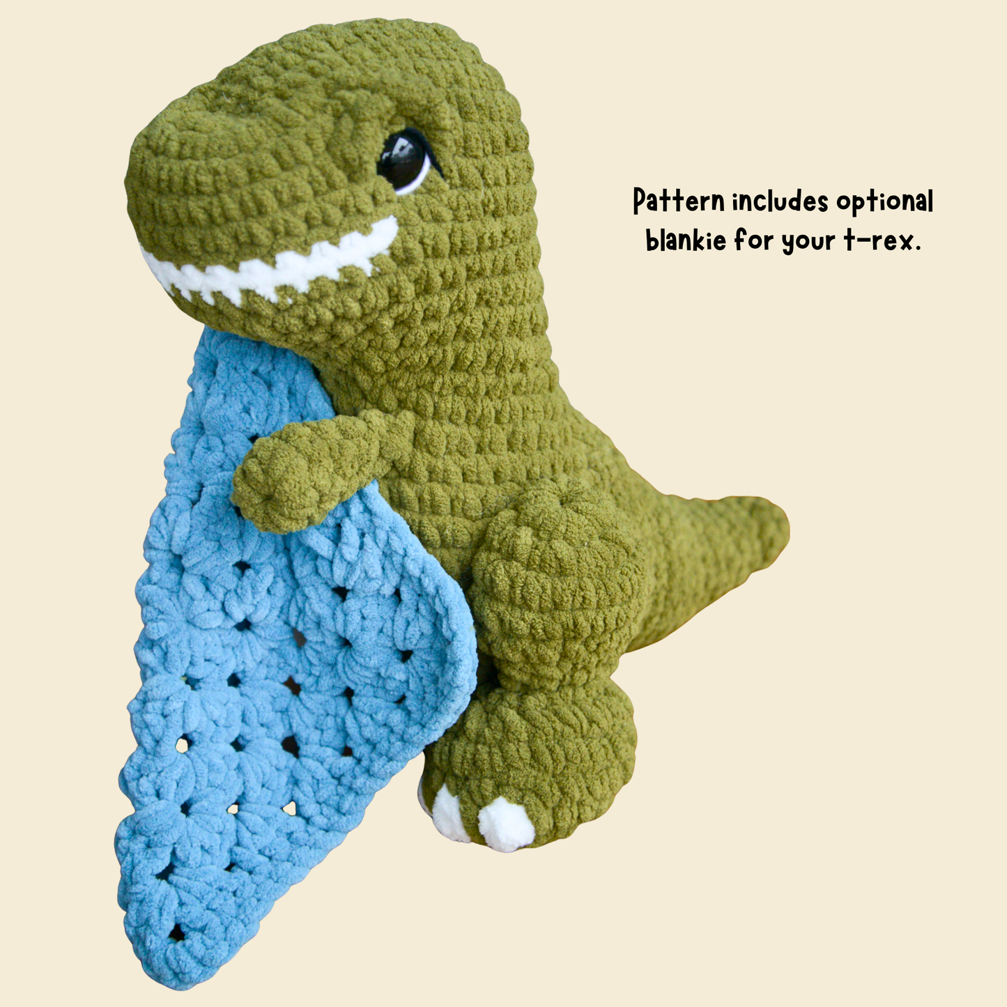 Crocheted dinosaur toy holding a blue blanket on a beige background