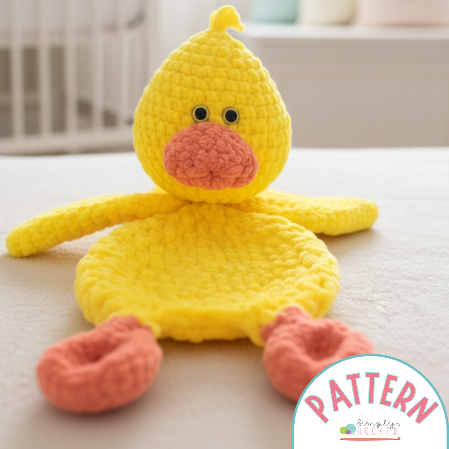 Yellow crocheted duck toy with pink beak and feet on a light surface, brand 'Simply Crochet' visible.