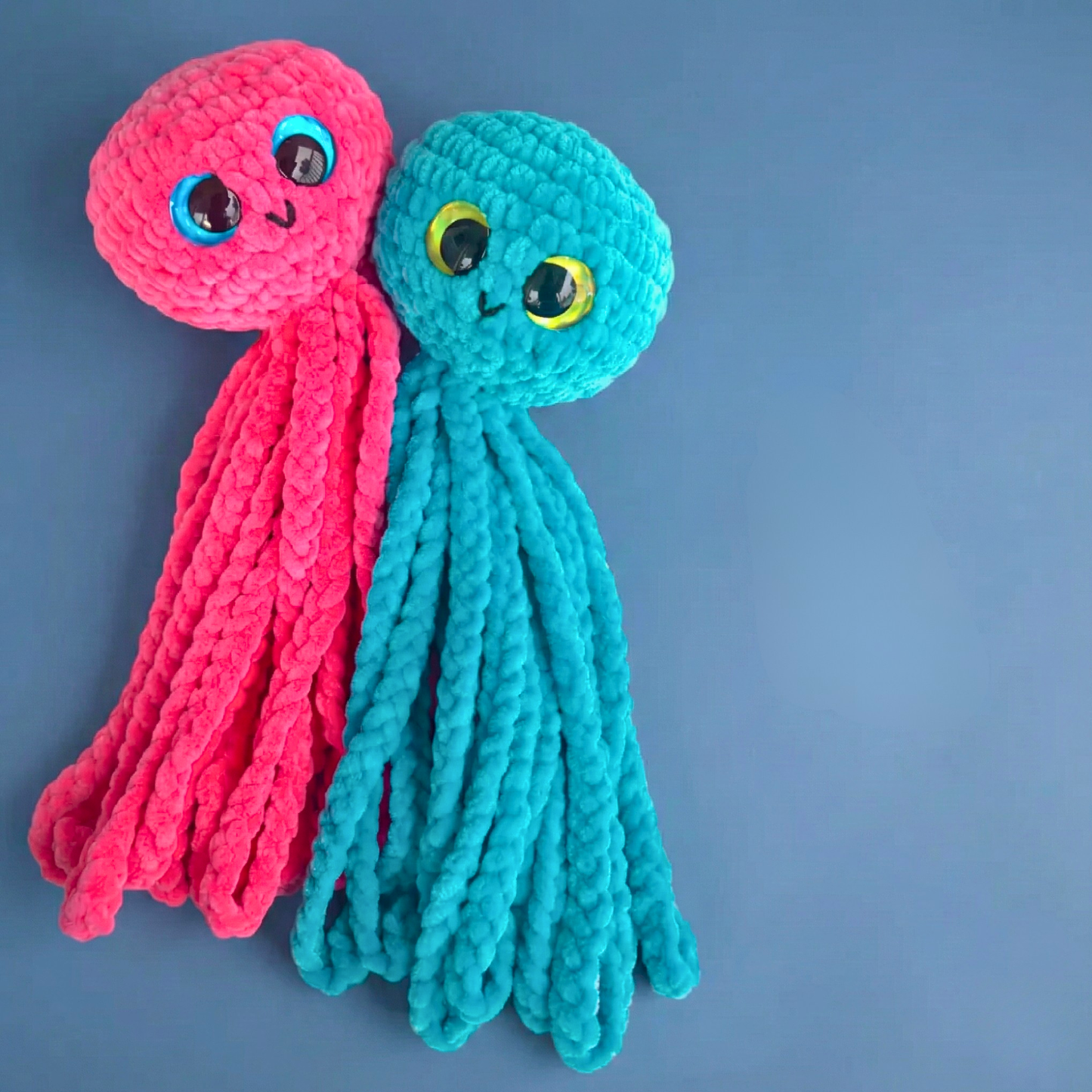 Pink and blue crochet jellyfish plushies with large eyes on a blue background