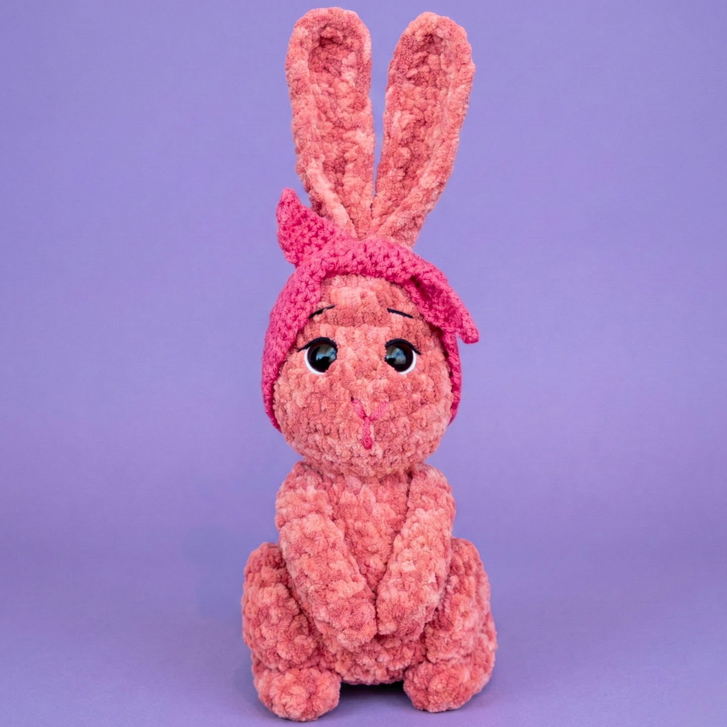 Pink knitted bunny toy on a purple background