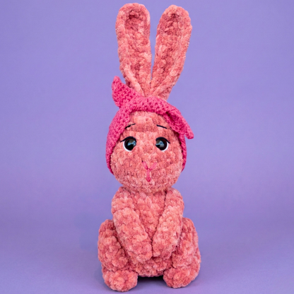 Pink knitted bunny toy on a purple background