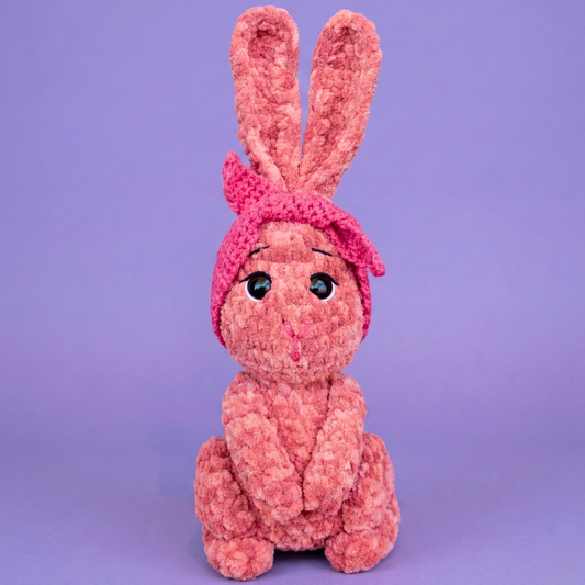 Pink knitted bunny toy on a purple background