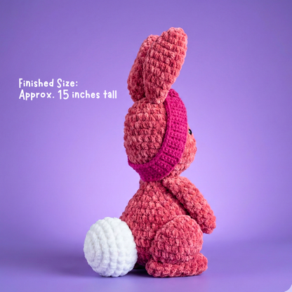 Crocheted pink bunny toy on a purple background with text indicating finished size.