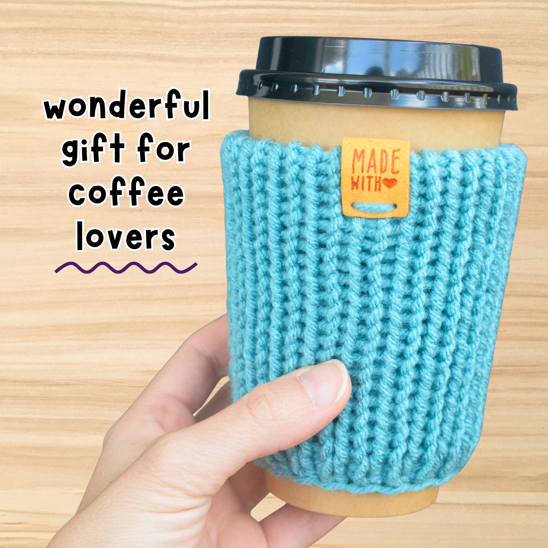 Hand holding a coffee cup with a blue knitted sleeve on a wooden background, labeled 'wonderful gift for coffee lovers'.