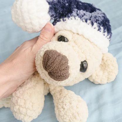 Hand holding plush crochet sleeping bear in blue and white hat, amigurumi pattern