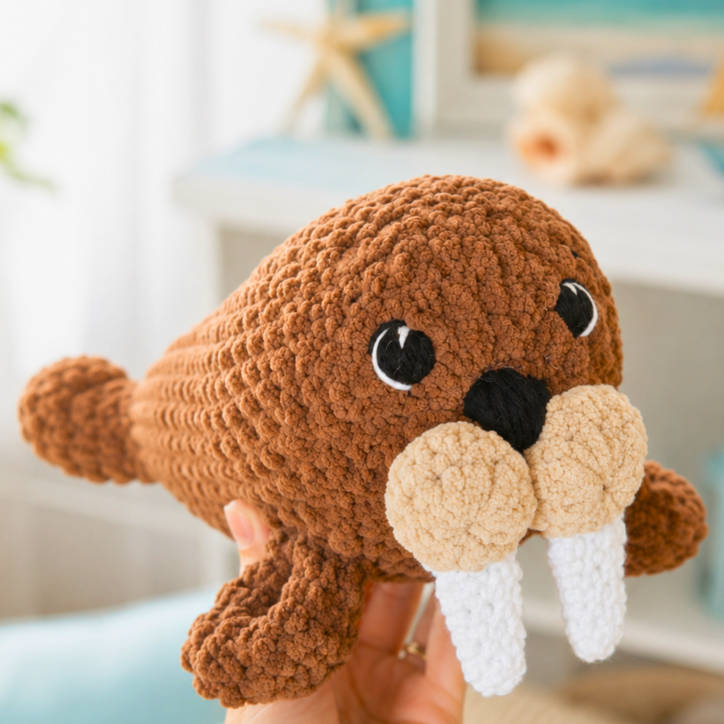 Crocheted walrus toy held by a person with a blurred indoor background