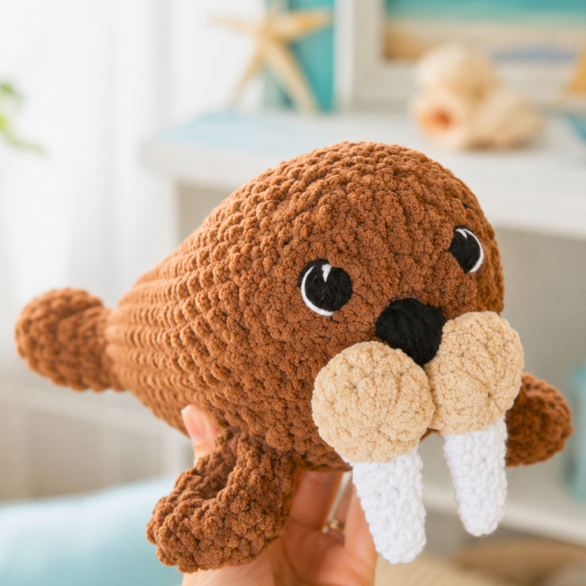 Crocheted walrus toy held by a person with a blurred indoor background