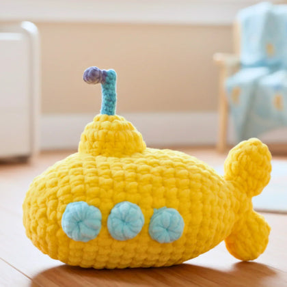 yellow submarine crochet amigurumi plushie with blue windows on a wooden floor