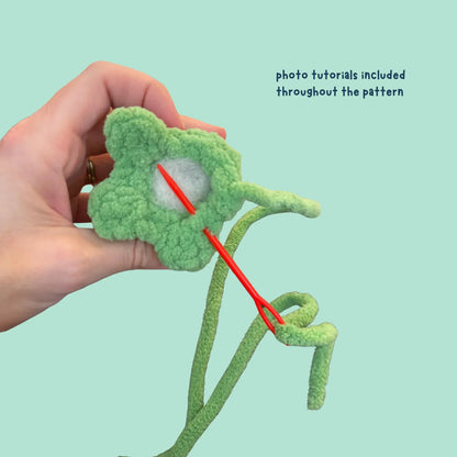 Hand holding green crochet flower, showing sewing technique with red yarn needle, amigurumi tutorial.