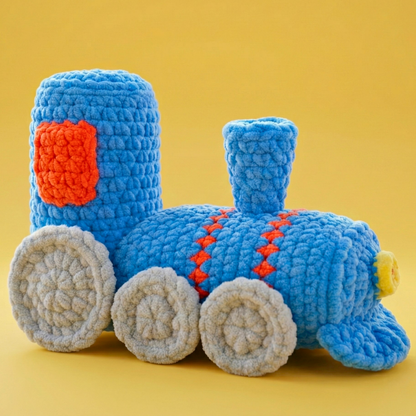 Plush blue crochet train with grey wheels and orange accents on yellow background