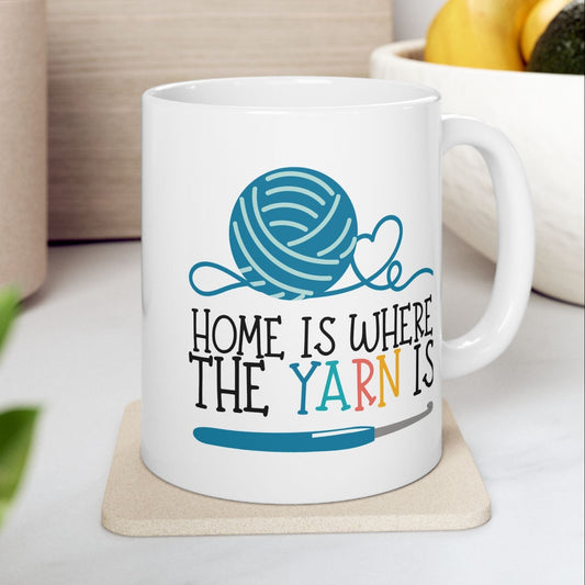 White mug with yarn design and text 'Home is where the yarn is' on a coaster.