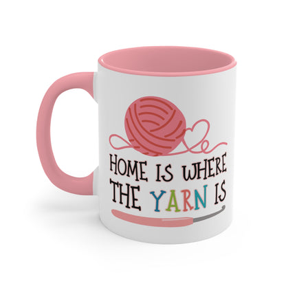 White mug with pink interior and handle, featuring a yarn ball design and text 'Home is where the yarn is' on a white background.