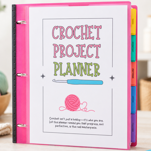 A pink and white ring binder 'Crochet Project Planner' displayed on a light wooden table with crochet hooks, yarn balls, and a plant in the background.