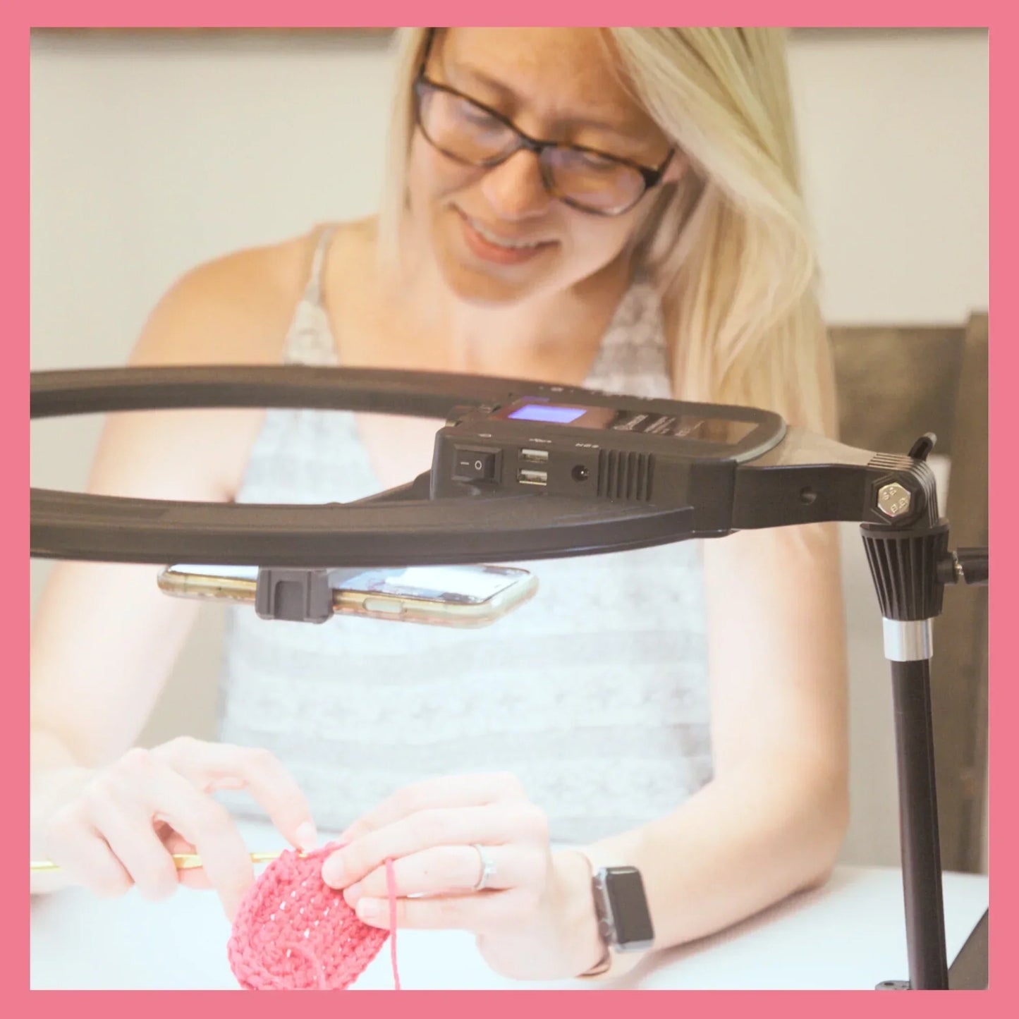 Woman filming a pink crochet project with a phone and ring light setup