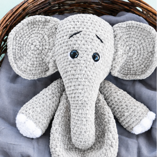 Promotional graphic for a crochet elephant pattern, featuring a gray crocheted elephant plush toy inside a wicker basket on a light mint background with text reading 'Perfect for Hugs' and 'Simply Hooked'.