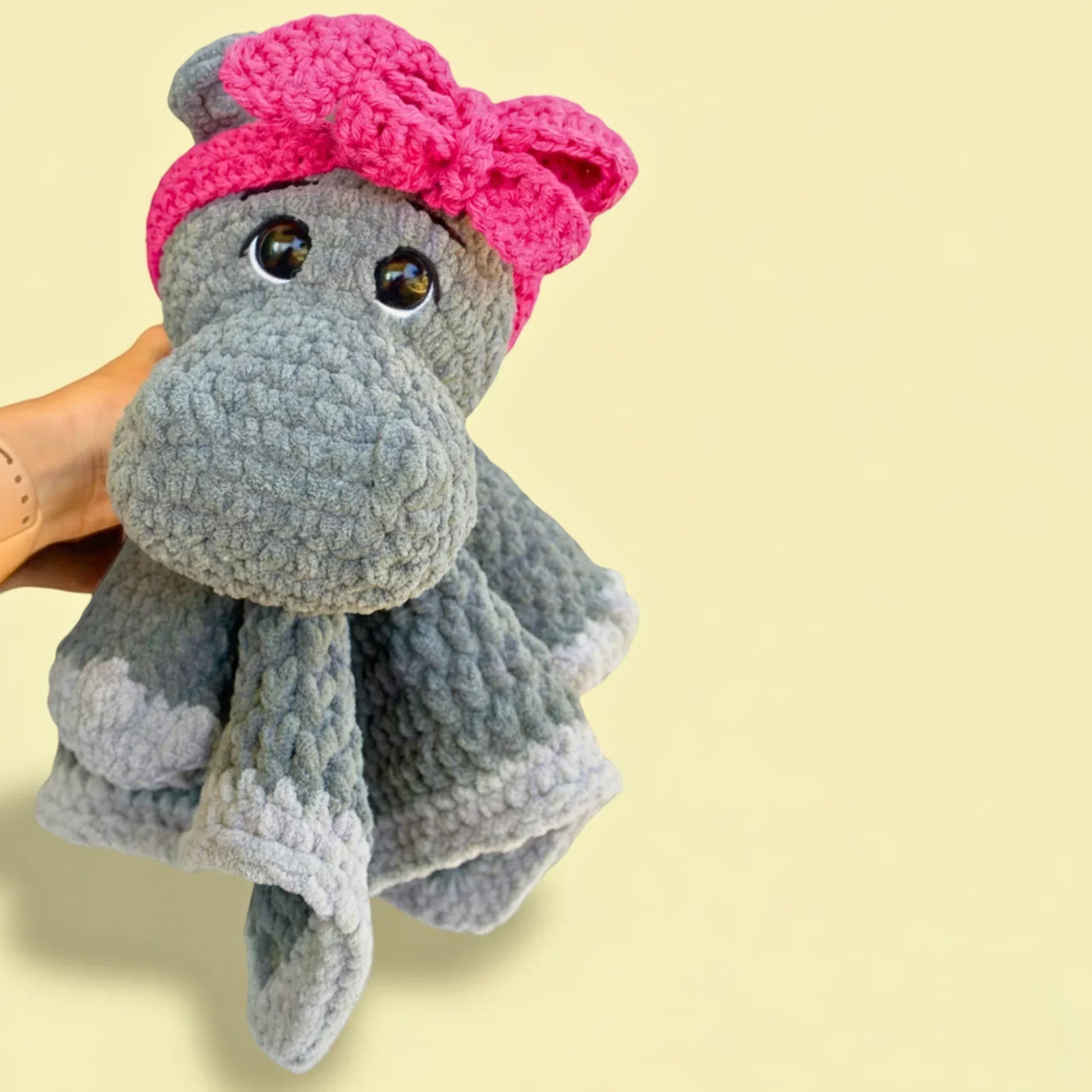 Hand holding a gray hippo crochet lovey with pink bow and plush blanket body