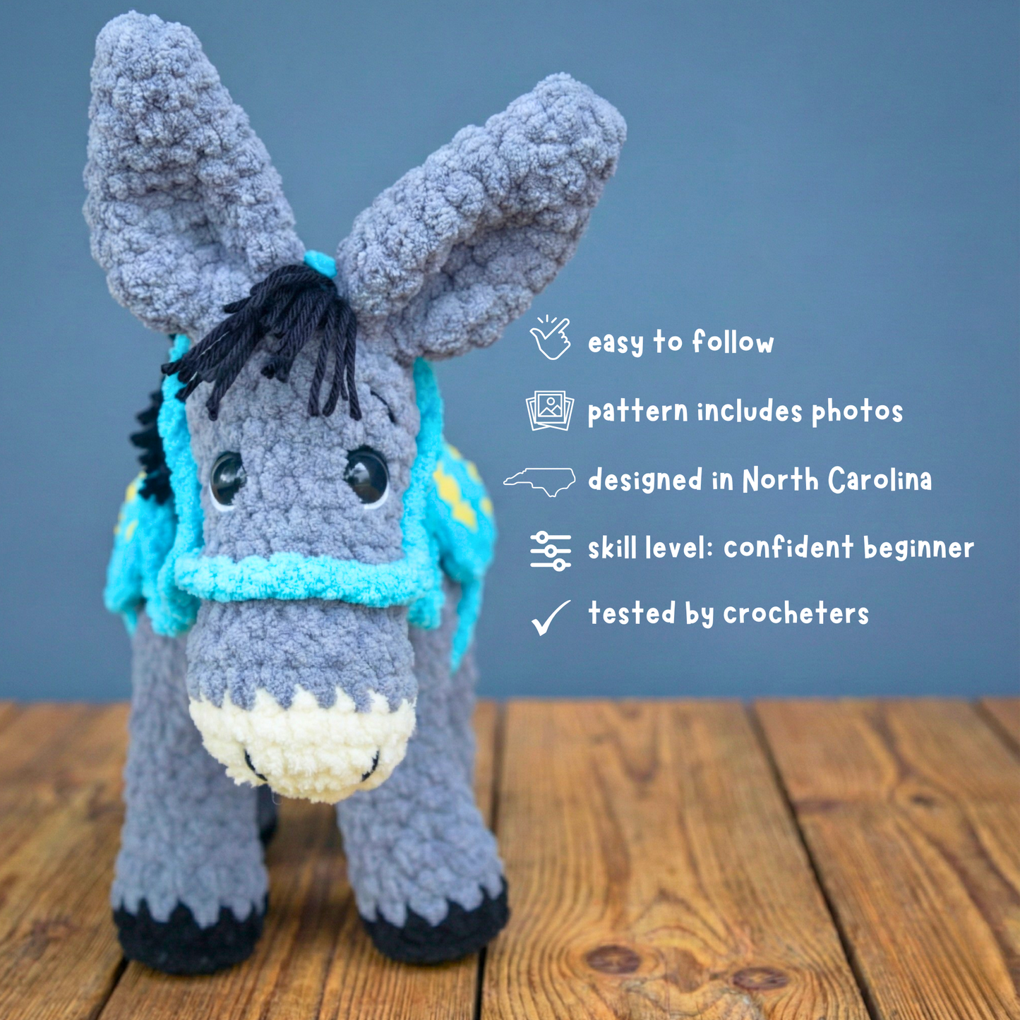 Grey crocheted donkey plush with blue harness on wooden surface, crafted with textured yarn