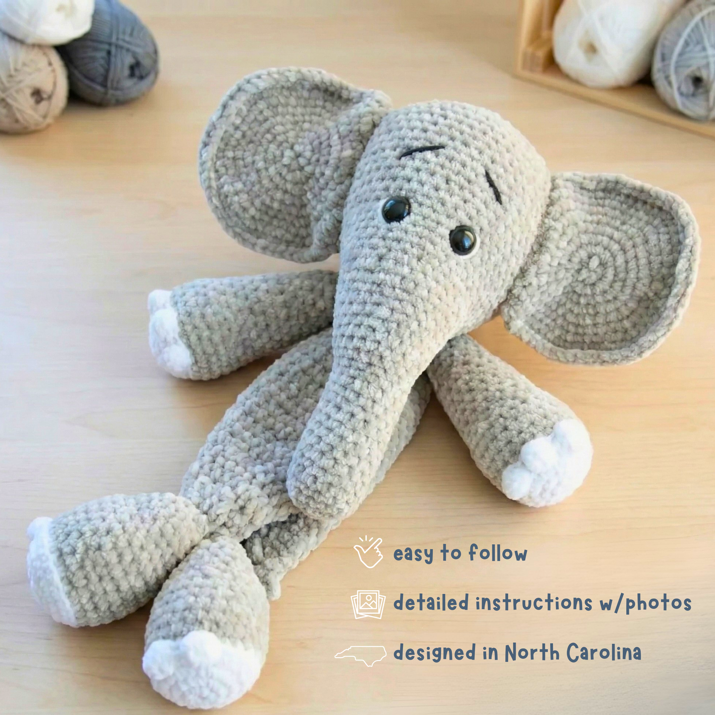 Gray crochet elephant plush toy with white accents on wooden surface and yarn in background