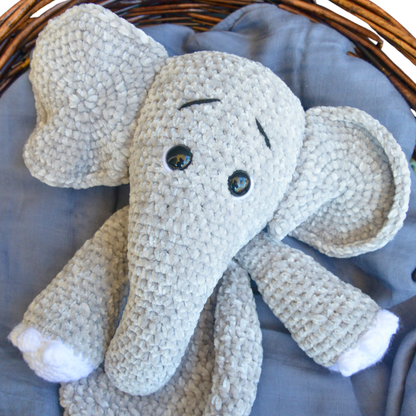Handmade crochet plush elephant toy with large ears and black eyes on blue fabric