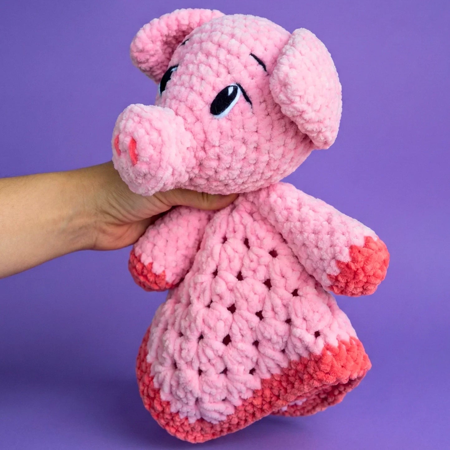 Hand holding a pink crochet pig plushie with a textured body on a purple background
