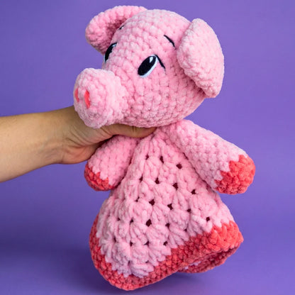 Hand holding a pink crochet pig plushie with a textured body on a purple background